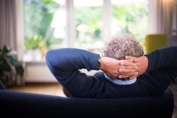 Man sitting on couch with hands behind his head.