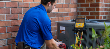 someone in a blue polo using a maintenance tool on an air conditioner