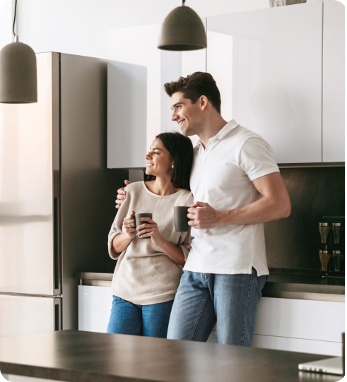 two people in the kitchen smiling and holding each other and coffee cups
